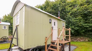 A small, single-story, green metal building with a wooden staircase leading to a door. - Shepherds Hut - The Crook (Milford Haven)
