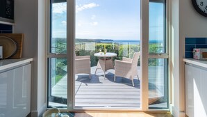 A modern kitchen with a large sliding glass door leading to an outdoor deck with wicker chairs and a small table. - Two Hoots (Kingsbridge)