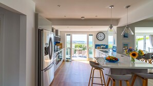 A modern kitchen with stainless steel appliances, a large island with bar stools, and a view of the outdoors. - Two Hoots (Kingsbridge)
