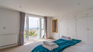 A bedroom with a large bed, a view of the sea through a sliding door, and a wardrobe with multiple doors. - Two Hoots (Kingsbridge)