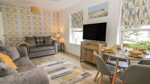 A modern living room with a grey sofa, a dining table with chairs, a TV, and a patterned wall. - The Krusty Krab (Filey)
