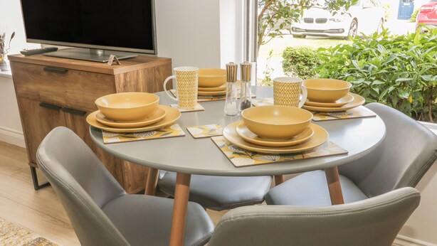 A dining area with a round table, grey chairs, and yellow bowls. - The Krusty Krab (Filey)