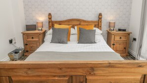 A neatly made bed with a wooden headboard, two bedside tables with lamps, and a small bedside table with a clock. - The Krusty Krab (Filey)