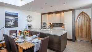 Et moderne køkken med en central ø, et spiseområde med et træbord og stole, et ur på væggen og en stor trædør.
