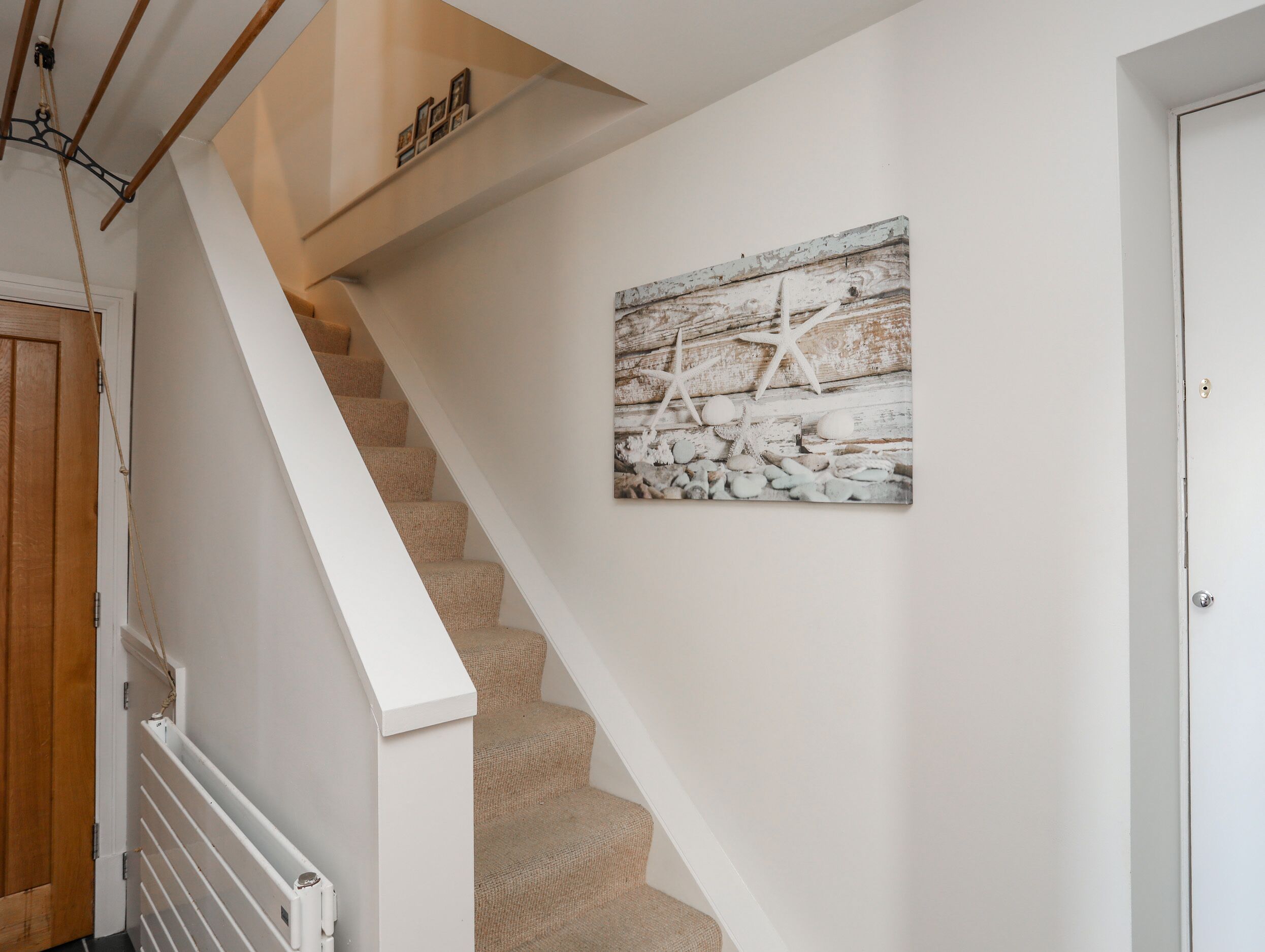 Un escalier avec une rampe blanche, une porte en bois et une œuvre d’art murale représentant des étoiles de mer et des pierres.