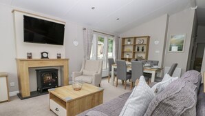A living room with a fireplace, a television mounted on the wall, a dining area with a table and chairs, and a bookshelf. - Cayton Pines (Scarborough)