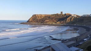 A coastal view with a cliff, beach, and a historic building on top. - Cayton Pines (Scarborough)