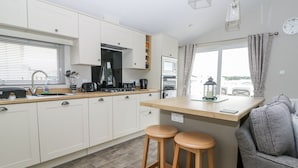 A modern kitchen with white cabinets, a wooden countertop, and two stools. - Cayton Pines (Scarborough)