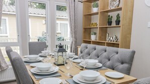 A dining table set for six with white plates, glasses, and cutlery, a lantern, and a grey upholstered chair. - Cayton Pines (Scarborough)