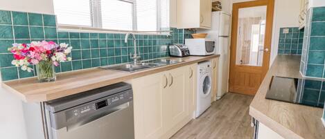 A modern kitchen with a dishwasher, washing machine, and a wooden countertop.