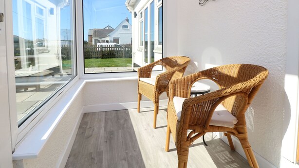 A sunlit room with two wicker chairs, a large window, and a white wall. - Senafe (Bude)