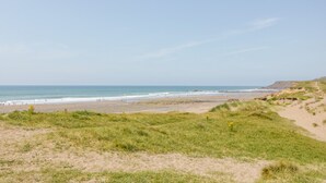A beach with a clear sky, sandy dunes, and a grassy area leading to the shore. - Senafe (Bude)