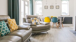 A modern living room with a leather sofa, a dining area with a table and chairs, and large windows with curtains. - Senafe (Bude)