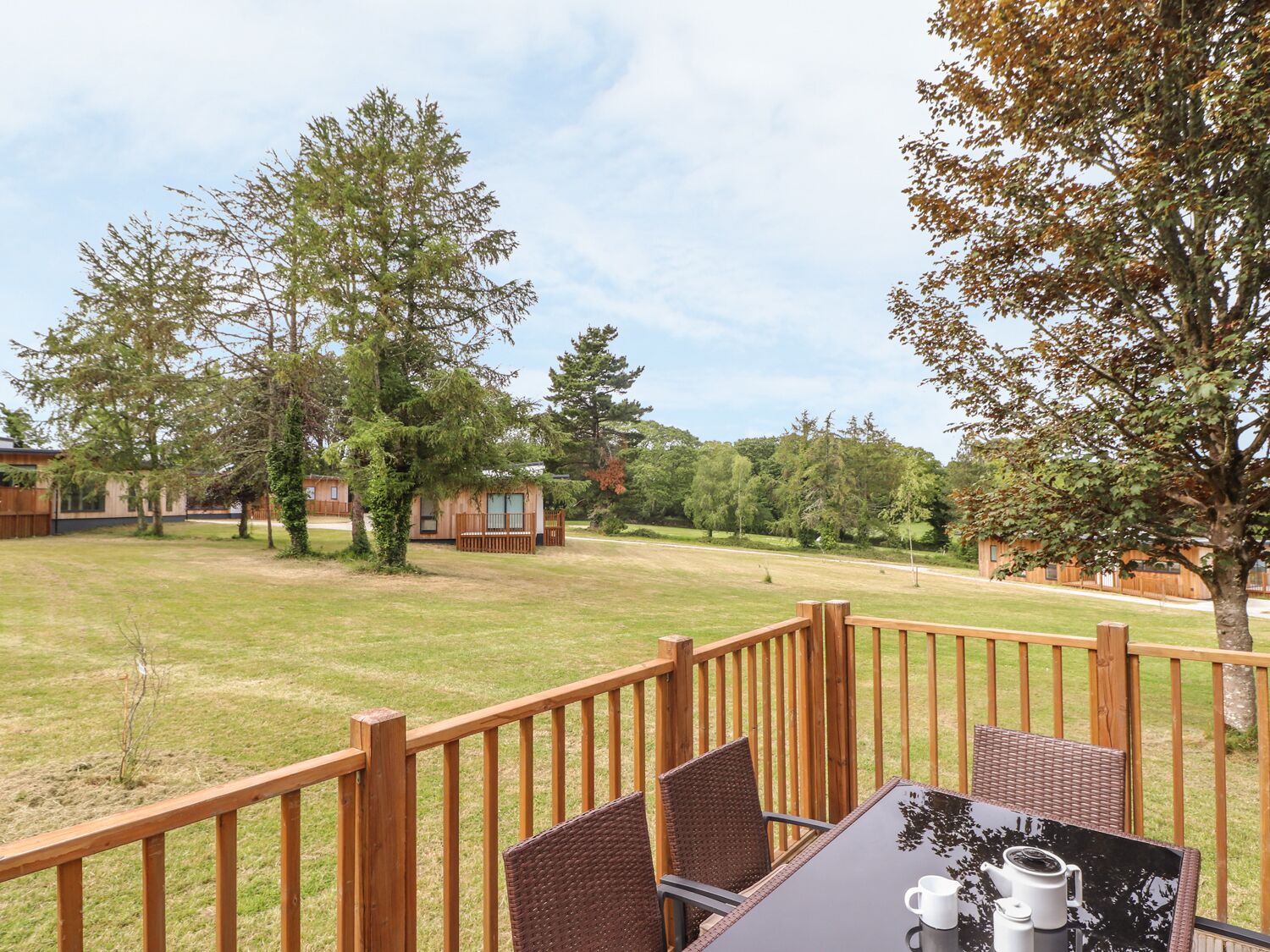 Une terrasse en bois avec une table et des chaises, donnant sur une zone verdoyante parsemée d’arbres et de cabanes.