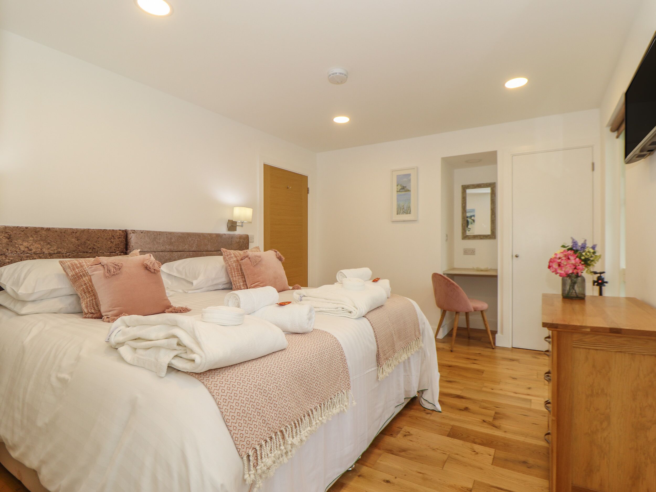 Habitación de hotel con una cama grande, un escritorio de madera, una silla y un televisor montado en la pared.