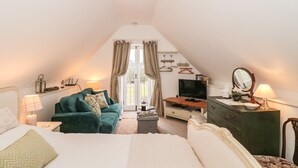 Une chambre confortable et bien éclairée, avec un grand lit, un fauteuil vert, une télévision et une commode.