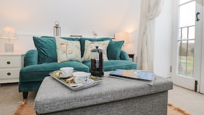 Une pièce chaleureuse avec un canapé turquoise, un pouf gris et un plateau contenant des éléments pour le petit-déjeuner.