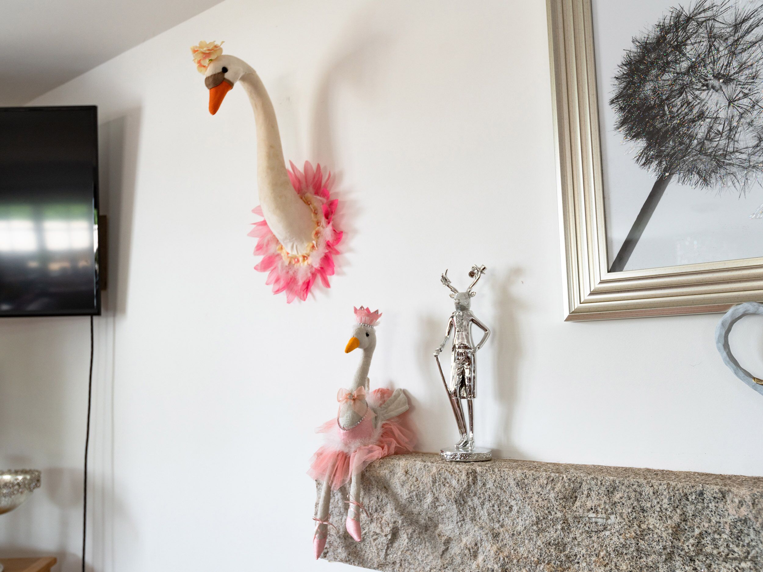 A wall with a mounted TV, a framed artwork, and two decorative items on a mantelpiece.