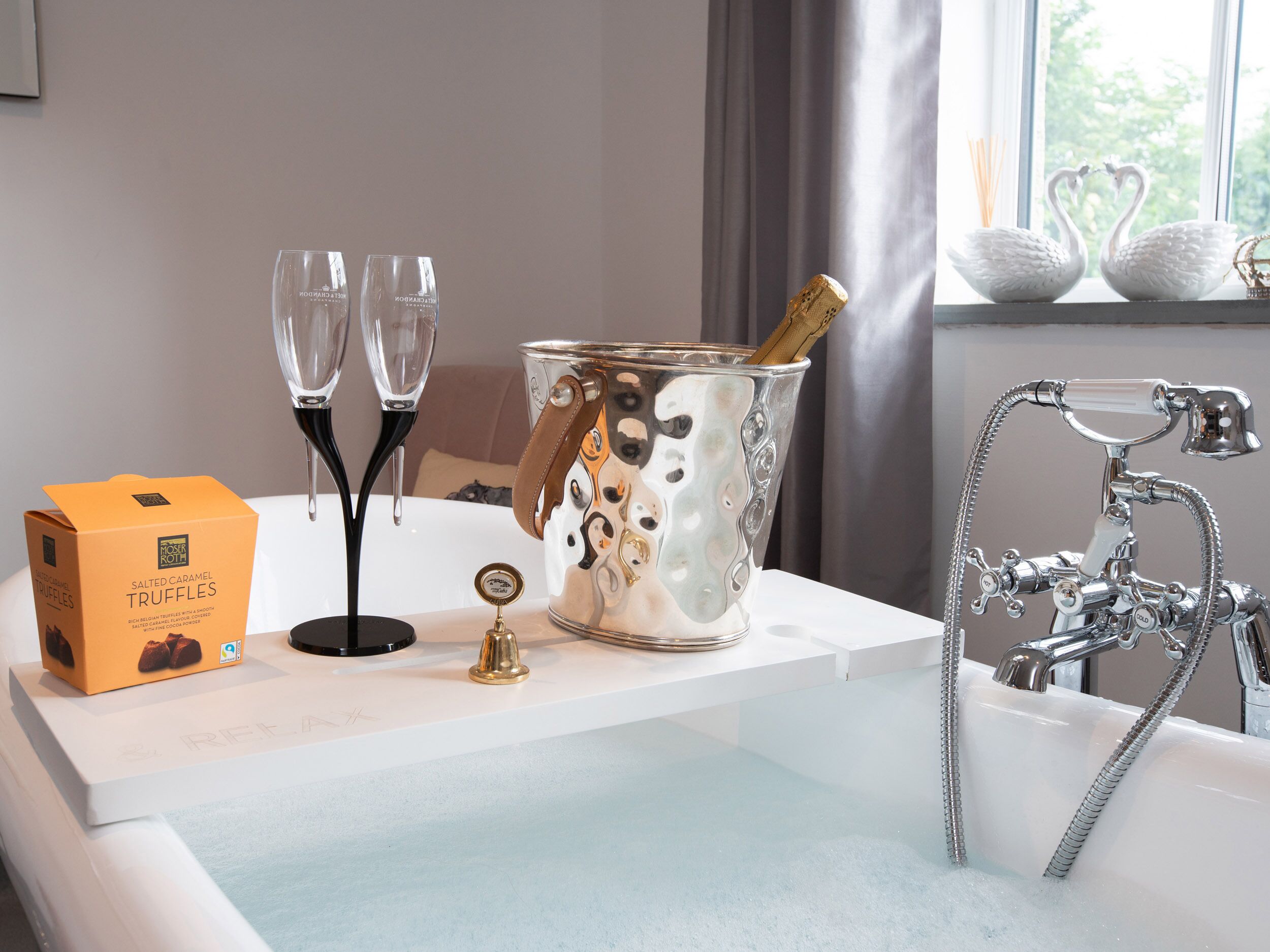 Une salle de bain avec une baignoire, un robinet de style rétro et un récipient en métal décoratif contenant une bouteille de champagne.