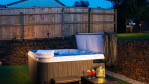 A hot tub with a wooden exterior, a bench, and a lantern on a grassy area. - Be Our Guest Cottage (Truro)