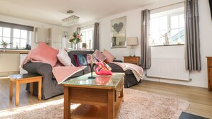 A modern living room with a glass coffee table, a sofa, and a dining area in the background. - Be Our Guest Cottage (Truro)