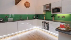A modern kitchen with white cabinets, a green backsplash, a built-in microwave, and a wooden beam ceiling. - Repton @ Engine Shed (Whitby)