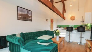 A cozy living room with a green sofa, a small table with a vase, and a kitchen in the background. - Repton @ Engine Shed (Whitby)