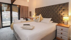 A bedroom with a large bed, a wooden headboard, a bedside table with a lamp, and a view through a glass door. - Repton @ Engine Shed (Whitby)