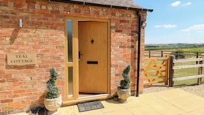 A brick cottage with a wooden door, a sign reading "TEAL COTTAGE", and two potted plants outside. - Teal Cottage (Melton Mowbray)