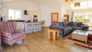 A spacious living area with a sofa, a plaid armchair, a coffee table, and a kitchen with a central island. - Teal Cottage (Melton Mowbray)