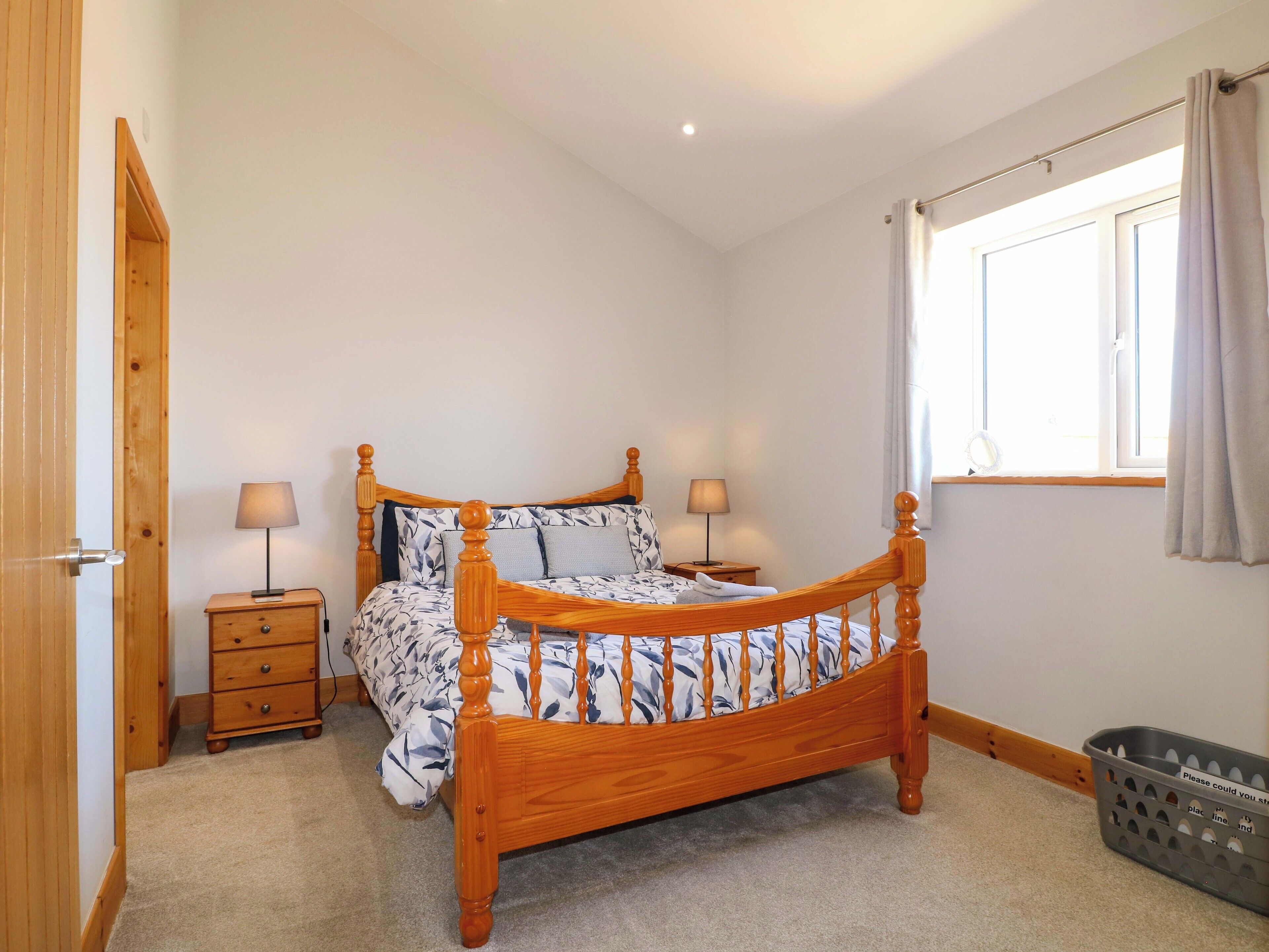Une chambre à coucher avec un lit à baldaquin en bois, une table de chevet avec une lampe, une petite commode et une fenêtre avec des rideaux.