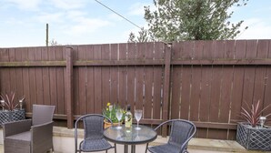 An outdoor patio with a round table and four wicker chairs, surrounded by a wooden fence and potted plants. - Gough Bank (Bridlington)