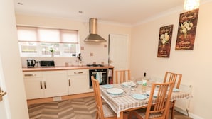A kitchen with a dining area, featuring a herringbone floor pattern, wooden chairs, and a table set for four. - Gough Bank (Bridlington)