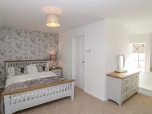 A bedroom with a bed, a bedside table with a lamp, a dresser, and a mirror.