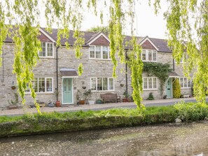 A stone building with multiple windows and doors, a bench, and a small garden area with potted plants. - Duck Cottage (Weymouth)