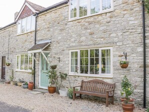 A stone building with multiple windows, a door, and a bench. There are potted plants around the building.