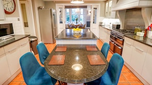 A modern kitchen with a central island, blue chairs, and a chandelier.