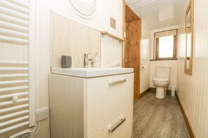 A compact bathroom with a white sink, wooden door, and a toilet. - The Lily Pad (Camborne)