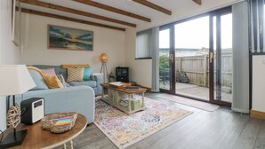 A living room with a sofa, a coffee table, a lamp, a radio, and a view through a glass door to the outside. - The Lily Pad (Camborne)