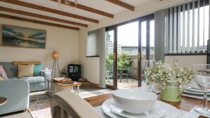 A living room with a sofa, coffee table, and dining table set with plates and glasses. - The Lily Pad (Camborne)
