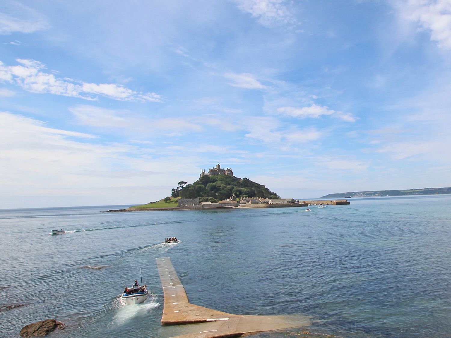 A coastal scene with a castle on a hill, a pier extending into the water, and boats.