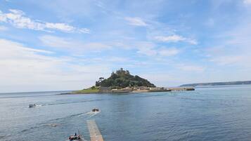 A coastal scene with a castle on a hill, a pier extending into the water, and boats.