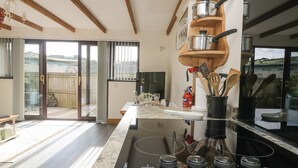 A modern kitchen with a central island, wooden shelves above the stove, and a sliding glass door leading to a backyard. - The Lily Pad (Camborne)