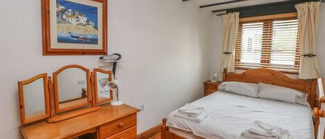 A bedroom with a wooden bed, a wooden desk with drawers, a mirror, a framed painting, and a window with curtains.