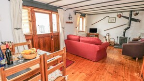 A cozy living room with a wooden floor, a red sofa, a dining table with chairs, and a fireplace. - Cowslip Cottage (Milford Haven)