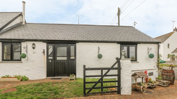 A white house with a black door and windows, a brick driveway, and a wooden gate. - Cowslip Cottage (Milford Haven)
