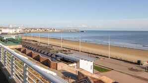 Um calçadão costeiro com uma praia, um muro marítimo e um cais ao longe.