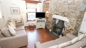 Un salon chaleureux avec une cheminée en pierre, deux canapés gris, un téléviseur et un mur en pierre.