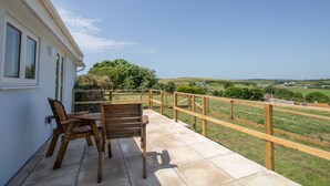 A patio with a table and chairs, a wooden railing, and a view of a green landscape. - Village View (Bridport)