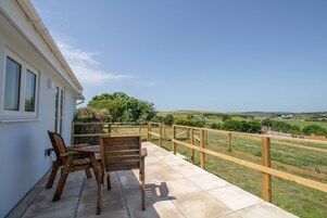 Un patio con mesa y sillas, barandal de madera y vista a un paisaje verde.
